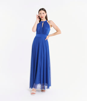 Donna con abito lungo bluette, colletto a nodo, pianta verde tropicale accanto