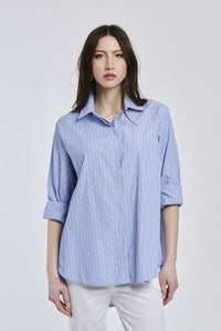 Donna con camicia a righe blu e bianche, colletto a camicia, maniche arrotolate a 3/4, taglio oversize.
