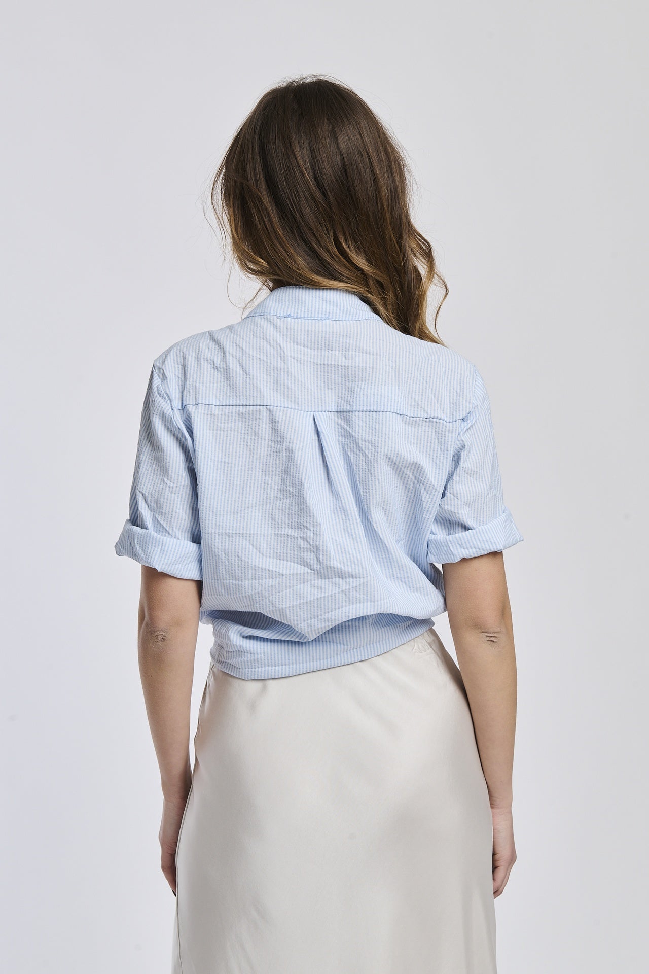 Camicia a righe azzurre da donna, maniche arrotolate e taglio cropped con nodo, ideale per un look estivo.