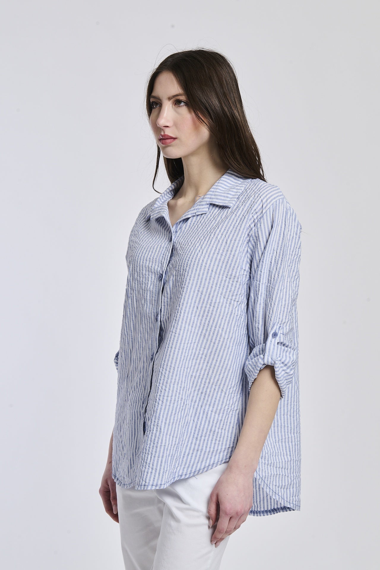 Donna con camicia a righe navy, oversize, colletto a camicia, bottoni frontali e maniche arrotolate.