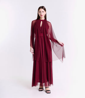 Abito vino rosso intenso, collo alto a nodo, pianta verde artificiale nel background