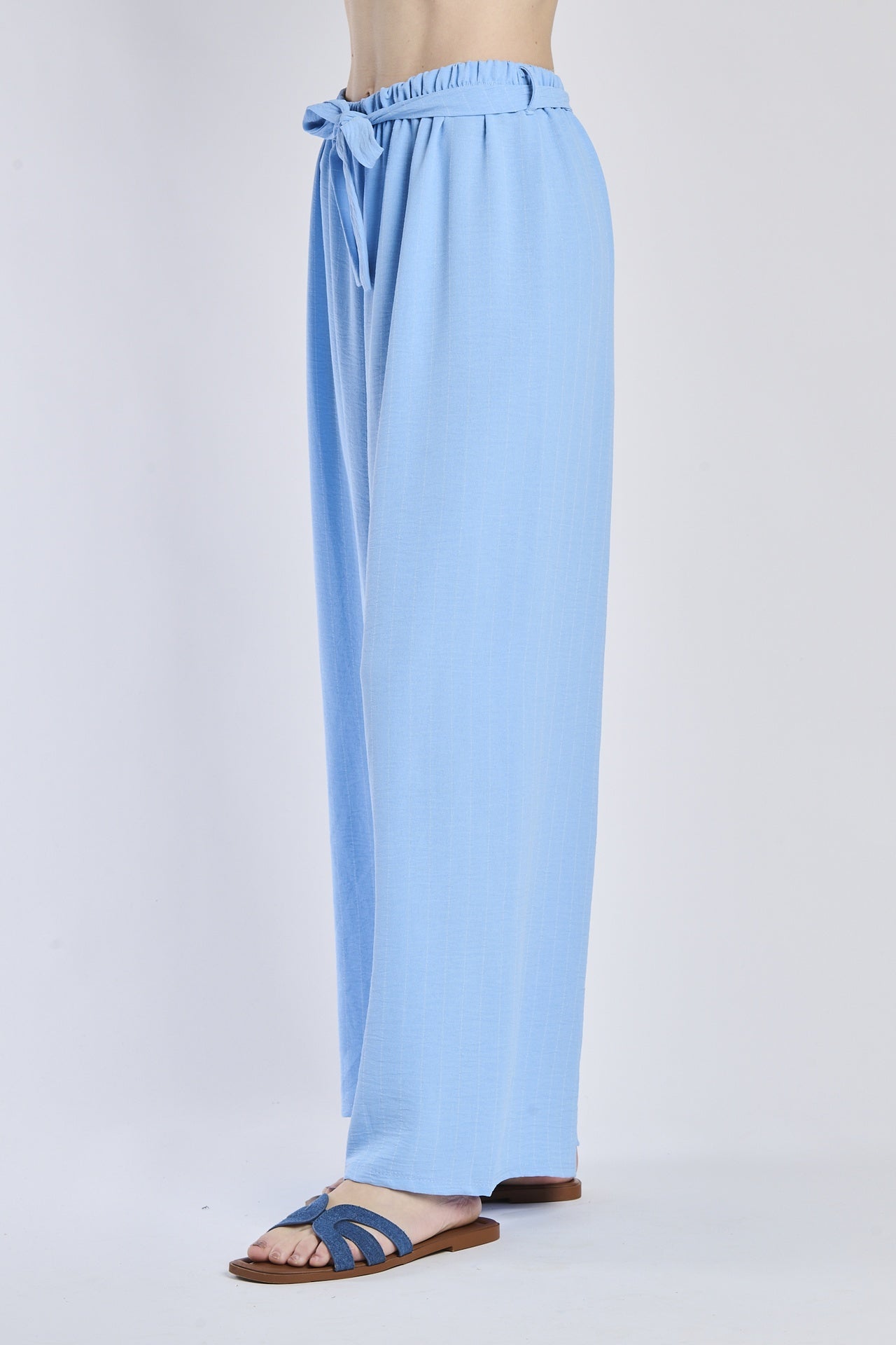 Pantaloni fluido azzurri, taglio ampio, nodo decorativo in vita, perfetti per l’estate.