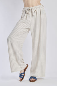 Pantaloni larghi beigi con coulisse e nodo in vita, abbinati a sandali.