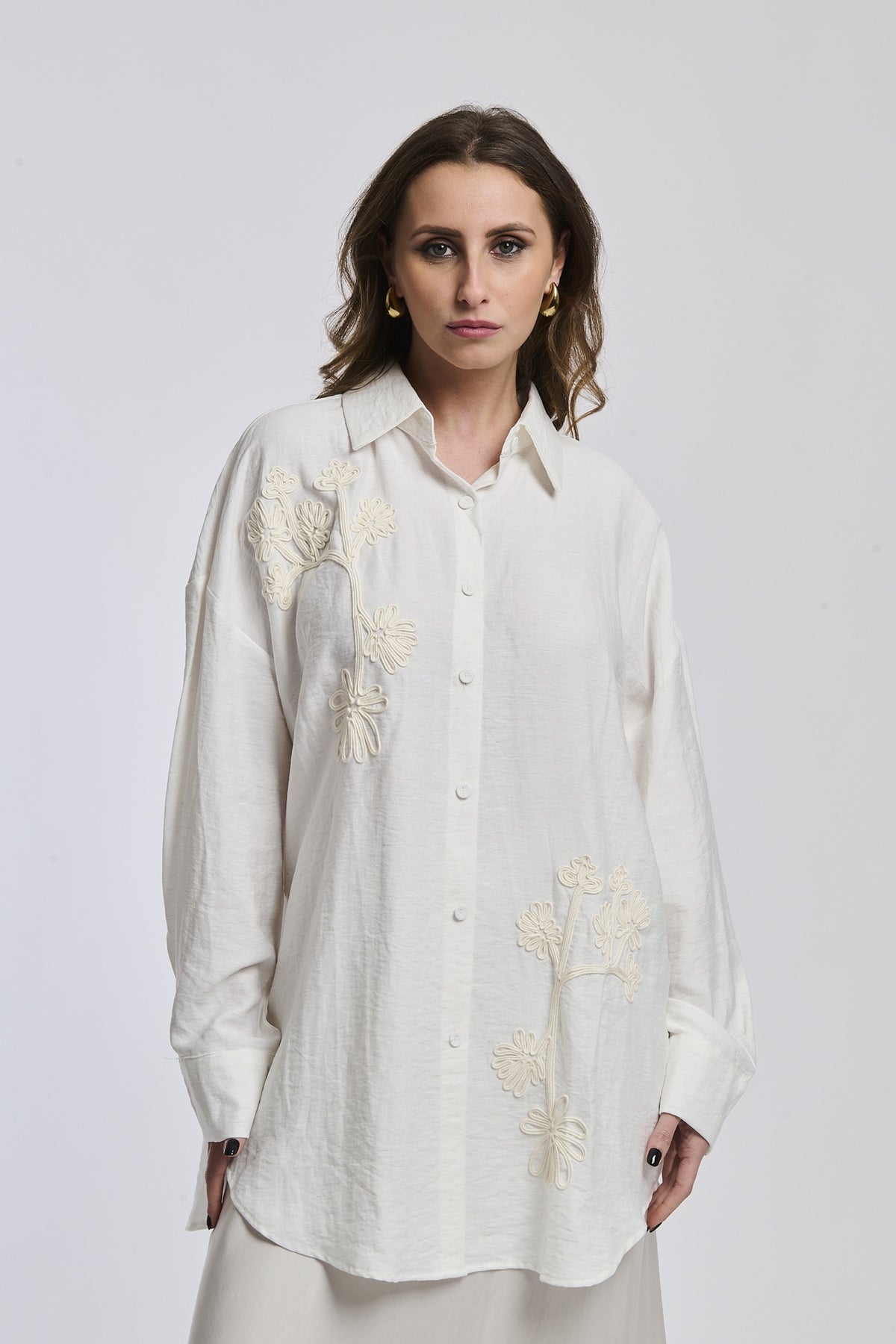 Una donna indossa una camicia di colore blu scuro intenso, con maniche lunghe e un leggero piegamento ai polsi, esprimendo un’aria di serietà e profondità.