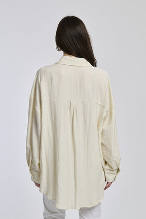 Donna veste una camicia di beige profondo, con colletto a mandarino e bottoni in legno, creando un look di elegante serietà.
