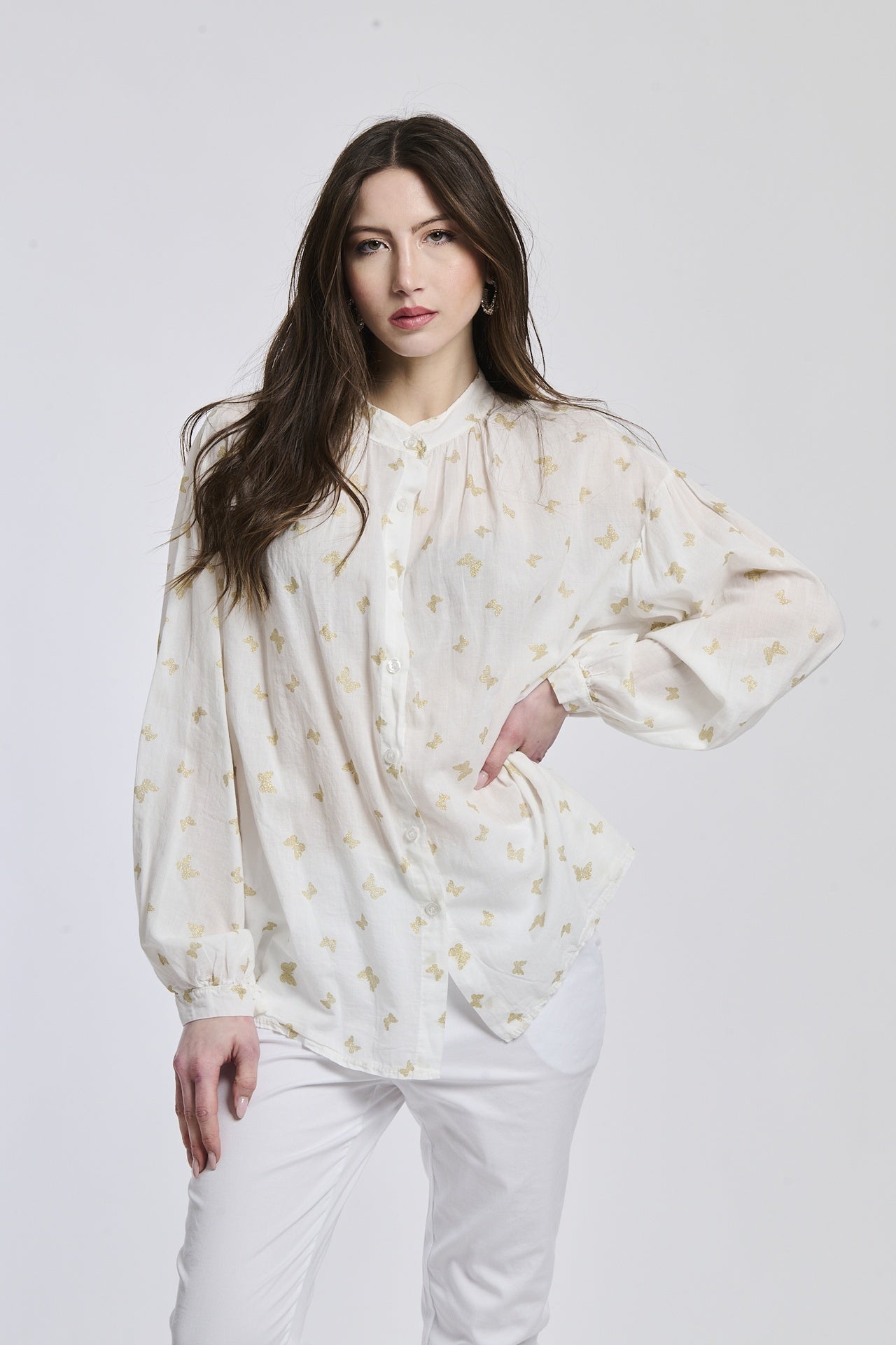 Donna indossa una camicia bianca stampata, maniche a lanterna, collo alto e bottoni centrali, stile pulito e romantico.