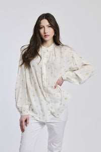 Donna indossa una camicia bianca stampata, maniche a lanterna, collo alto e bottoni centrali, stile pulito e romantico.