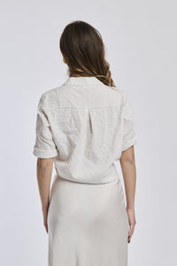 Donna indossa una camicia beige a righe, maniche corte e nodo decorativo, stile minimalista e accattivante.