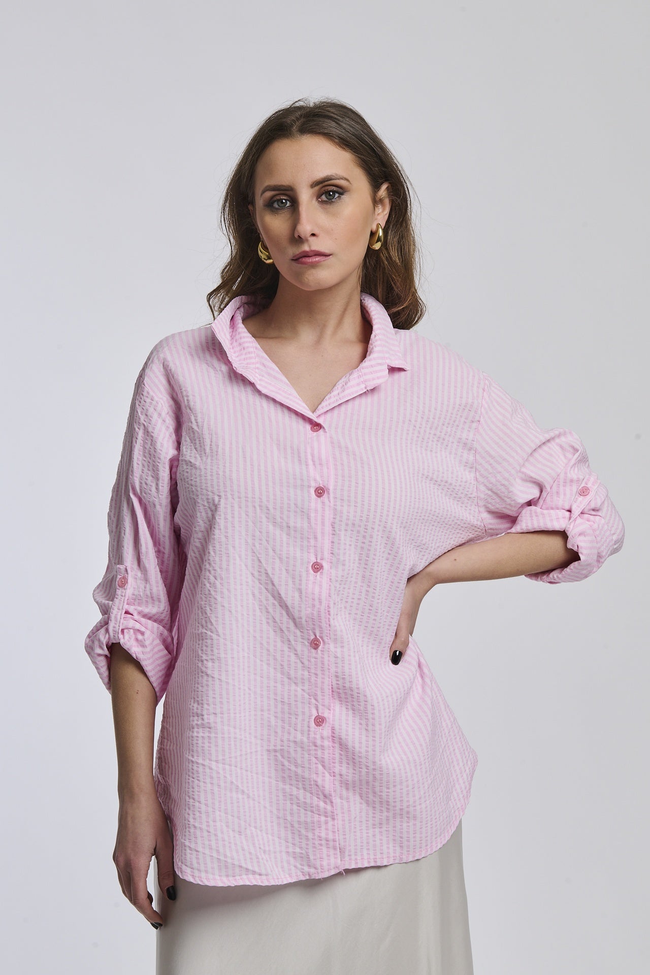 Donna con camicia a righe rosa, oversize, colletto a camicia, bottoni frontali e maniche arrotolate.