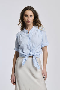 Donna indossa una camicia a righe azzurre e bianche, con il nodo sul basso, stile casual e fresco.