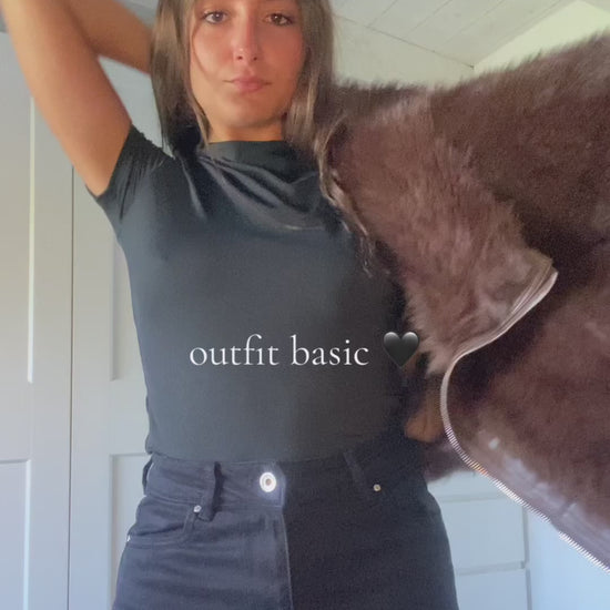 Modella con un look elegante: giacca in pelliccia marrone scura, top bianco e pantaloni neri, in posa stilizzata.