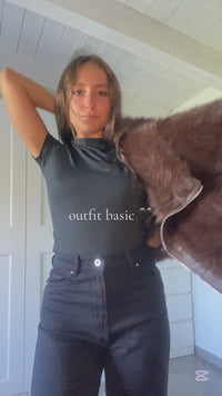 Modella con un look elegante: giacca in pelliccia marrone scura, top bianco e pantaloni neri, in posa stilizzata.