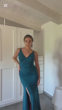  donna indossa un abito elegante blu scuro con spalline sottili e uno sguardo accattivante, posa in uno spoglio interno con armadio bianco sullo sfondo