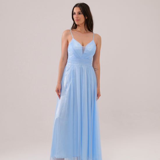 Donna con abito azzuro plissé e mantelle, posa sul lago con montagne sullo sfondo