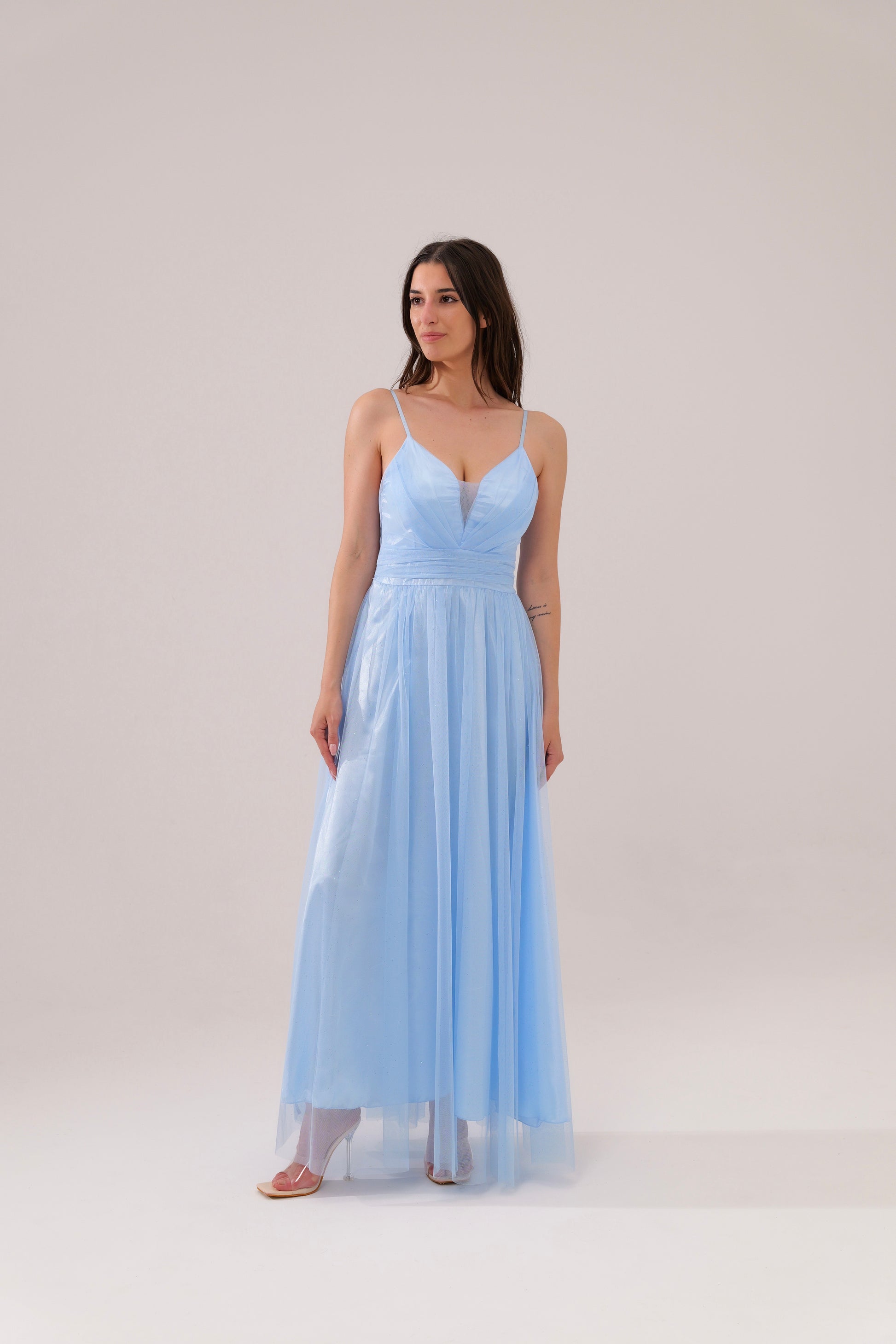 Donna con abito azzuro plissé e mantelle, posa sul lago con montagne sullo sfondo