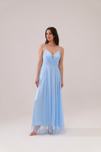 Donna con abito azzuro plissé e mantelle, posa sul lago con montagne sullo sfondo