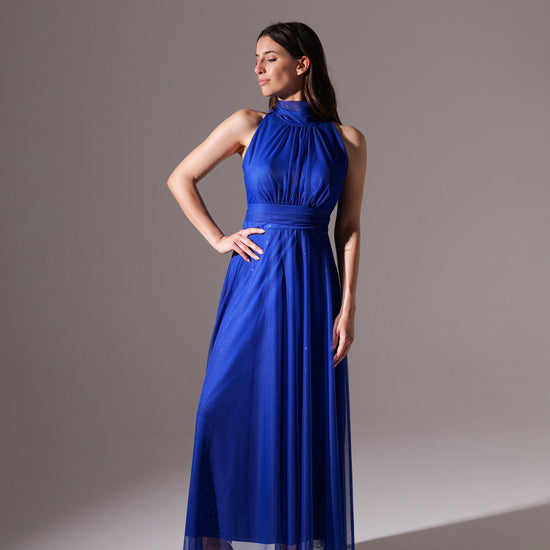 Donna in abito blu scuro fluido, colletto alto, posa con bracci alzati per esibire il vestito